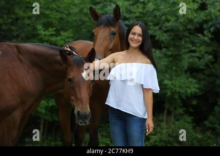 Hübsches Mädchen lächelt streichelt glatt das Pferd`s Mähne auf dem Feld. Zaum, Erwachsener. Stockfoto